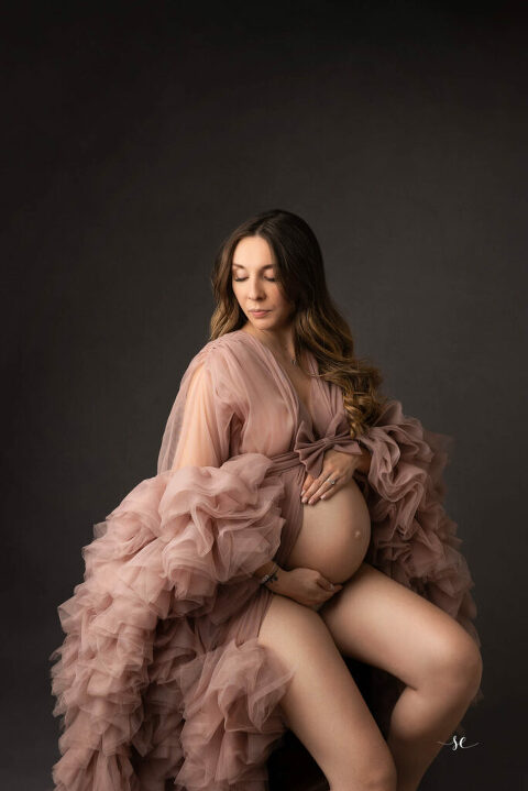 séance maternité dans le studio de Sabrina Esteves à Gaillon.Femme enceinte habillé d'une robe en tulle rose poudré sur fond gris.